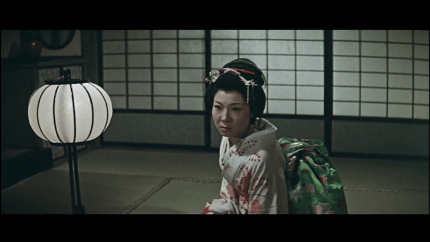 A woman in a traditional kimono sitting in a dimly lit room with a paper lantern.