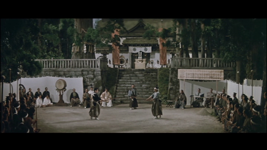 A traditional Japanese performance is taking place in an outdoor setting, with performers dressed in historical attire, a temple in the background, and an audience seated on both sides.
