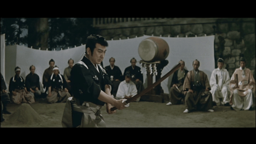 A samurai prepares to strike with a sword in a traditional Japanese setting, surrounded by seated spectators.