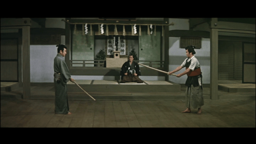 Two samurai engaging in a practice duel with wooden swords in a traditional dojo setting, while a spectator observes from the background.