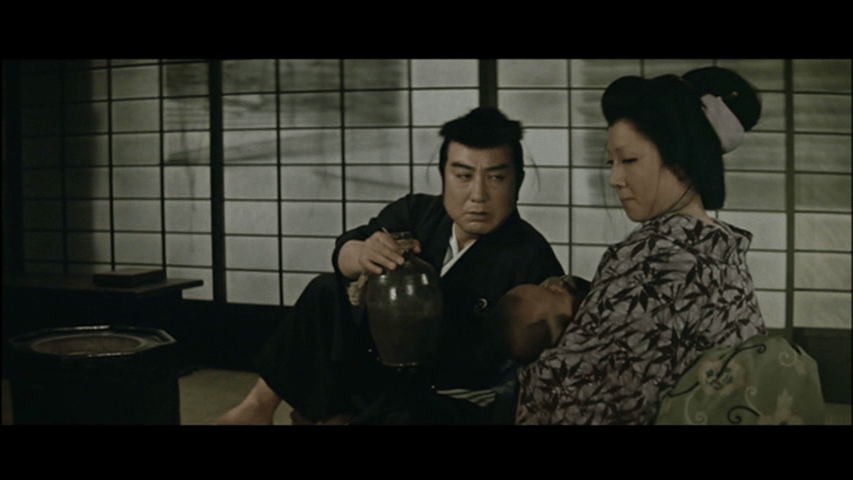 A traditional Japanese scene featuring a man and woman seated together, with the man holding a small jar, while a child rests in the woman's lap. The background shows shoji sliding doors.